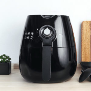 Black manual air fryer on a wooden table.