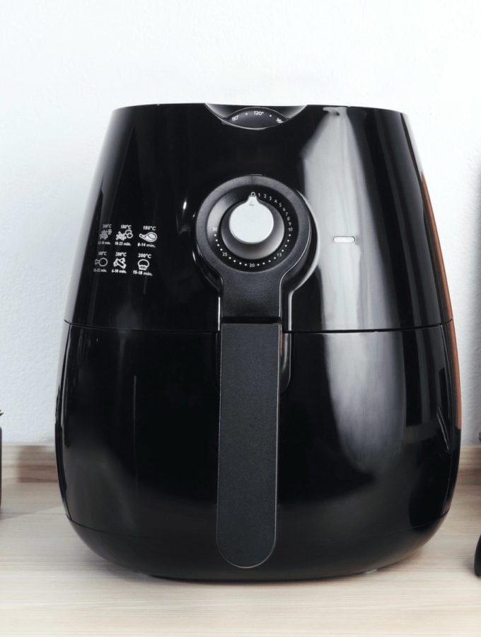 Black manual air fryer on a wooden table.
