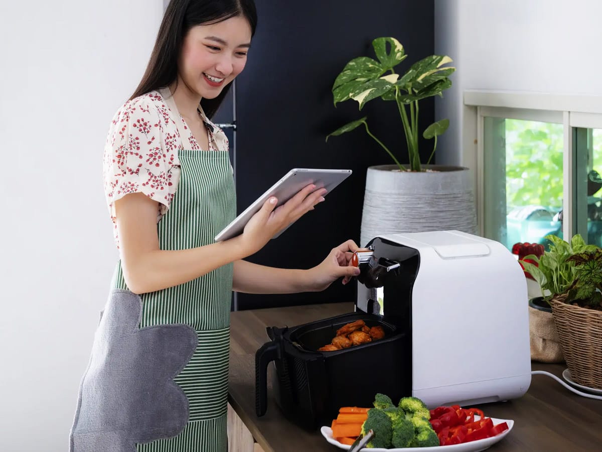 Girl looking on in iPad and setting the air fryer.