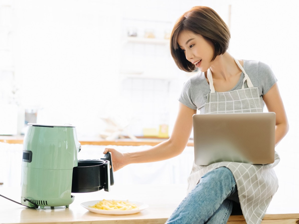 Girl with laptop holding the air fryer basket.