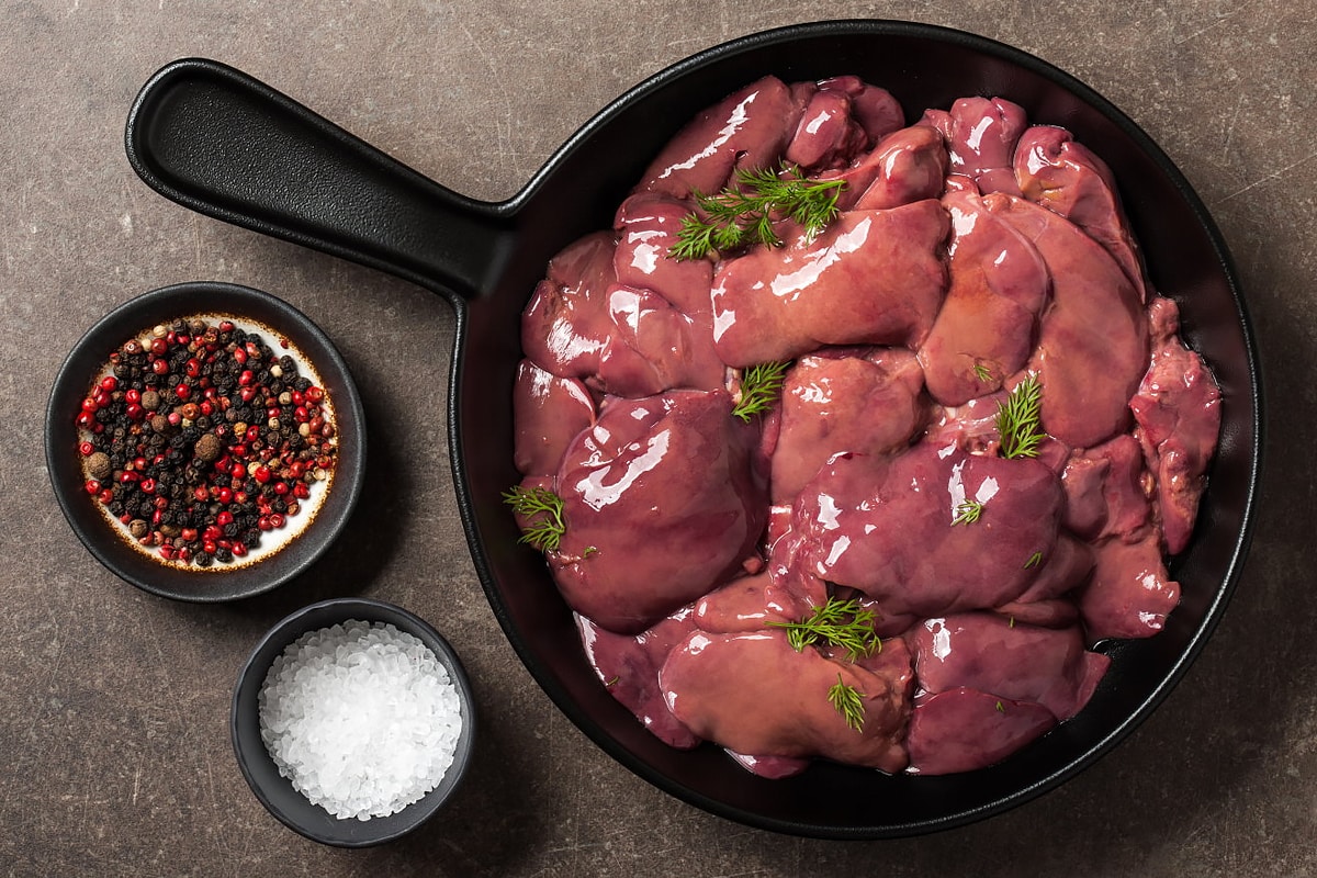 Top view of a pan with raw chicken livers with salt and pepper.