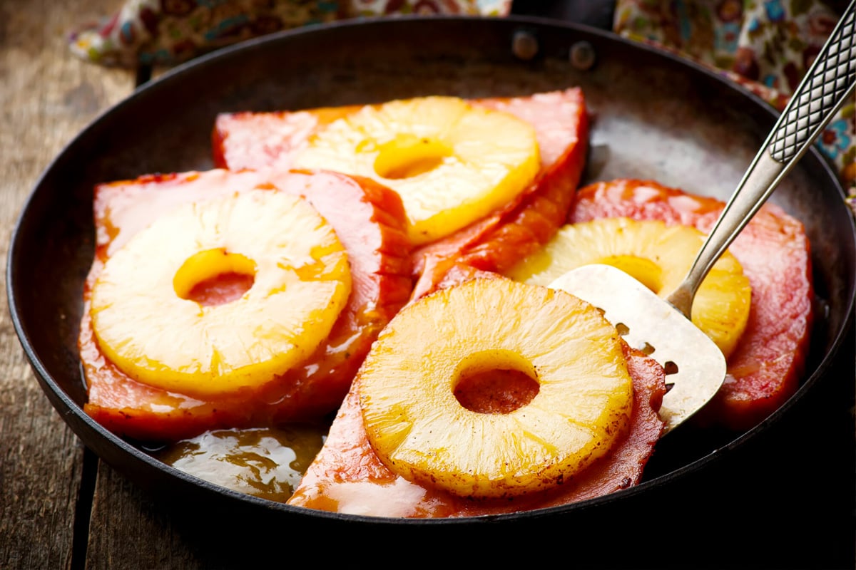 Sliced gammon reheating on a pan and covered with pineapple slices.
