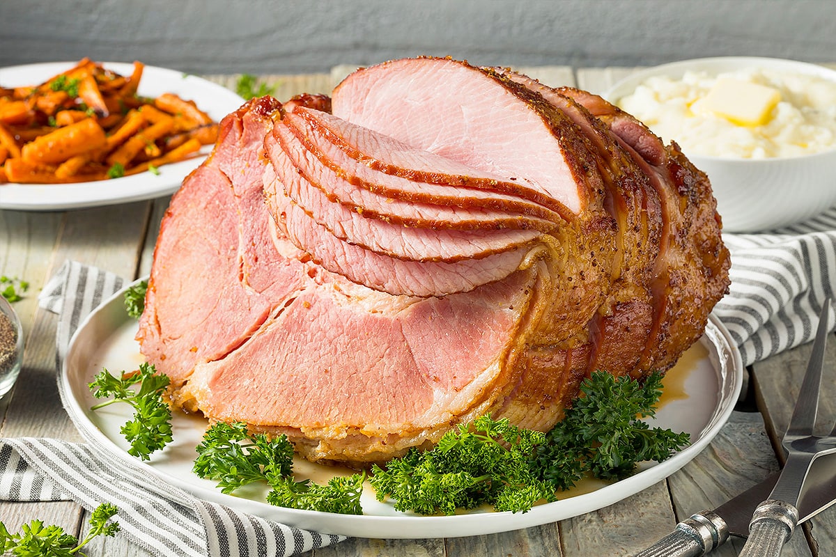 Sliced gammon with aromatic herbs and roasted carrots on background.