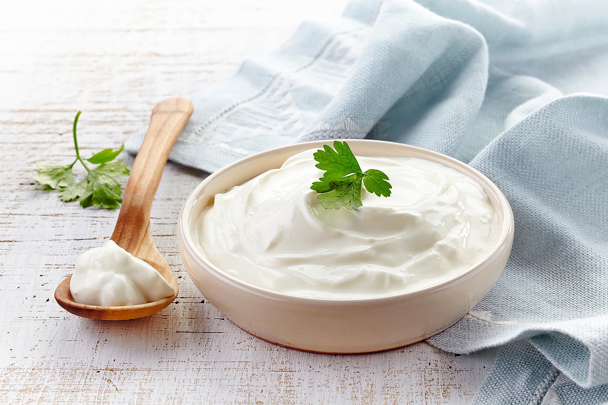 A wooden spoon and bowl with sour cream and parsley.