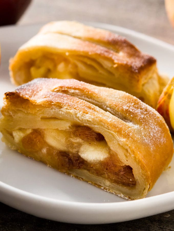 Close look of apple strudel in a white plate with apple slices.