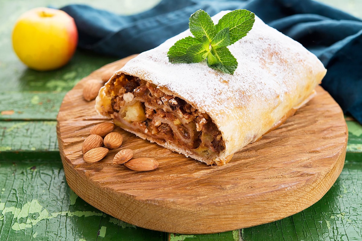 Apple strudel with nuts and powdered sugar on wooden table.