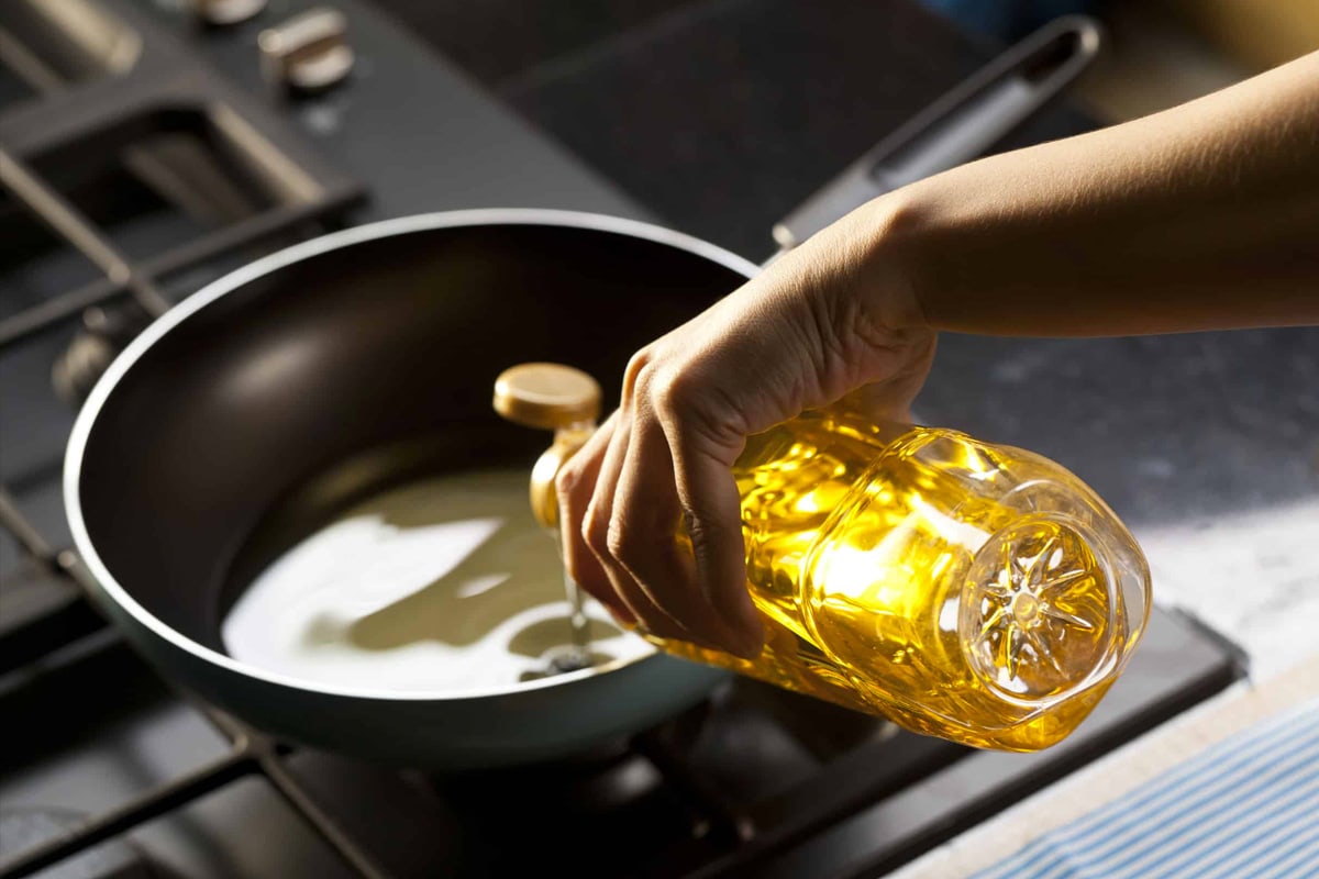 Woman hand pouring olive oil in a large deep pan.