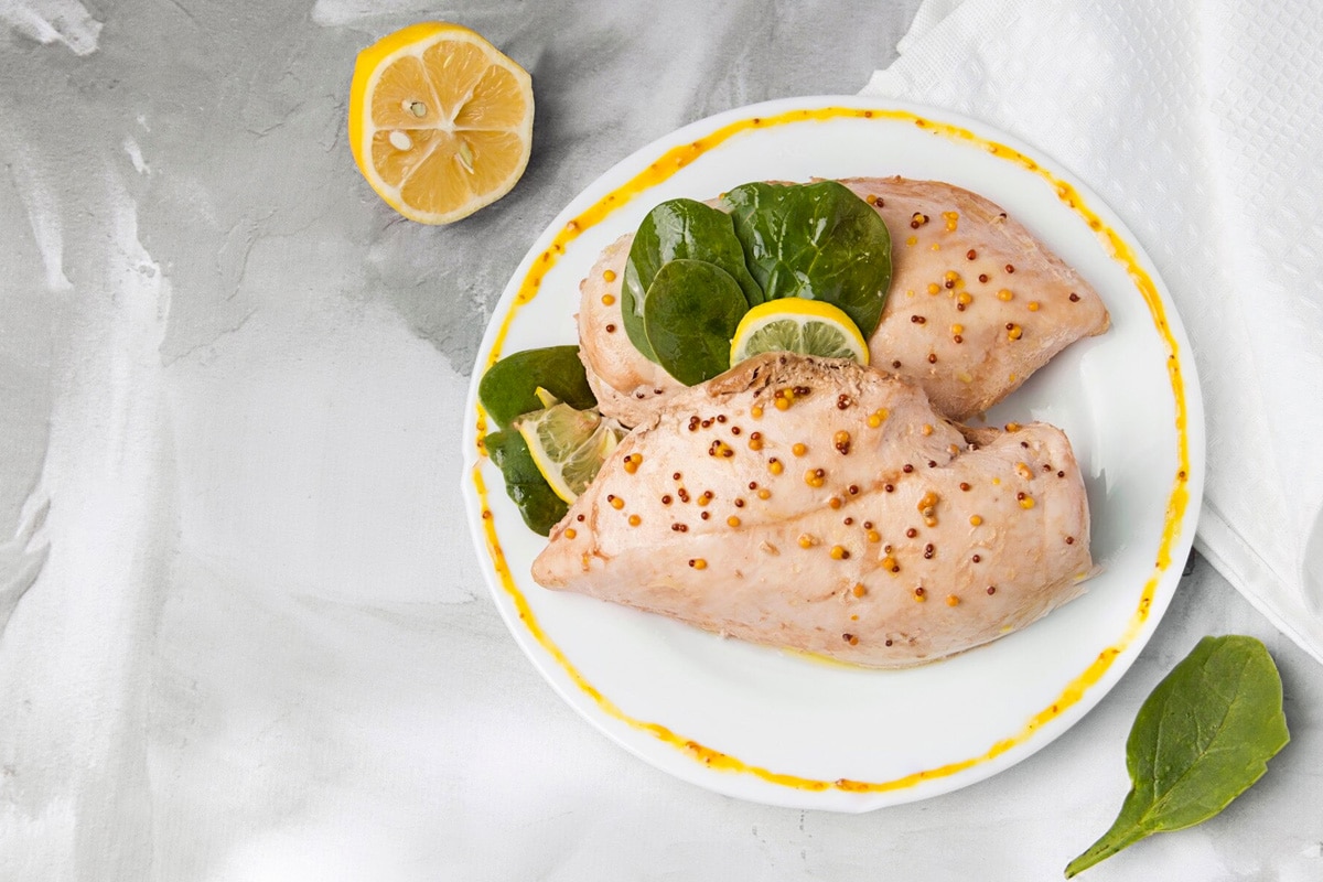Top view of marinated chicken breast with mustard and lemon slices.