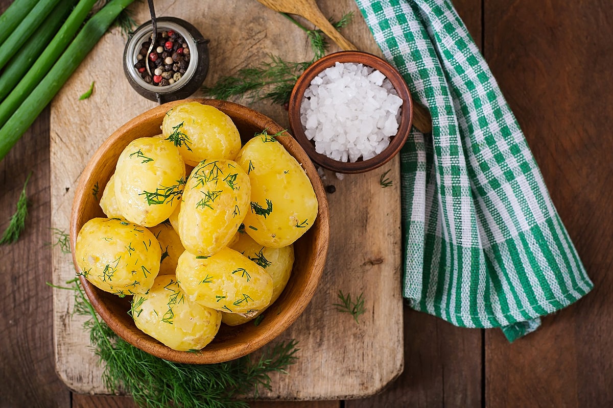Boiled potatoes with dill, salt, and black pepper on a wooden board.