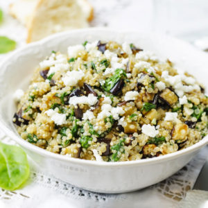 White plate with a quinoa salad with eggplant and salad leaves.