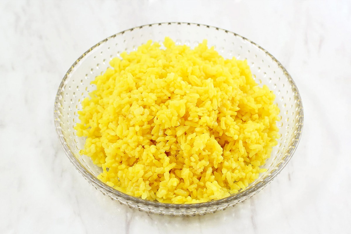 Transparent plate with cooked yellow rice on a white table background.