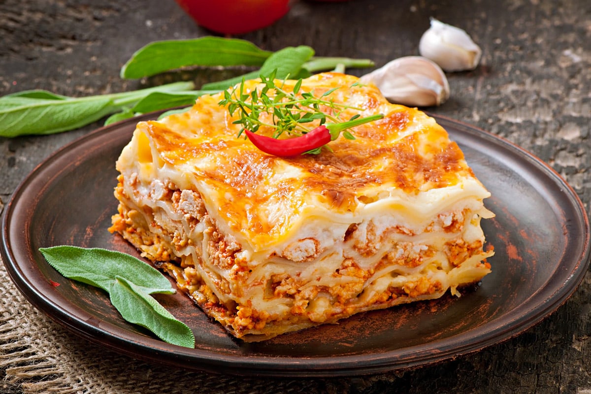 Close look of lasagna slice with red pepper on a rustic plate.