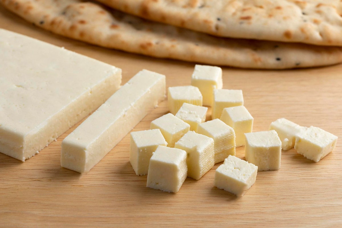 Close view of cubes of paneer cheese on a wooden table.