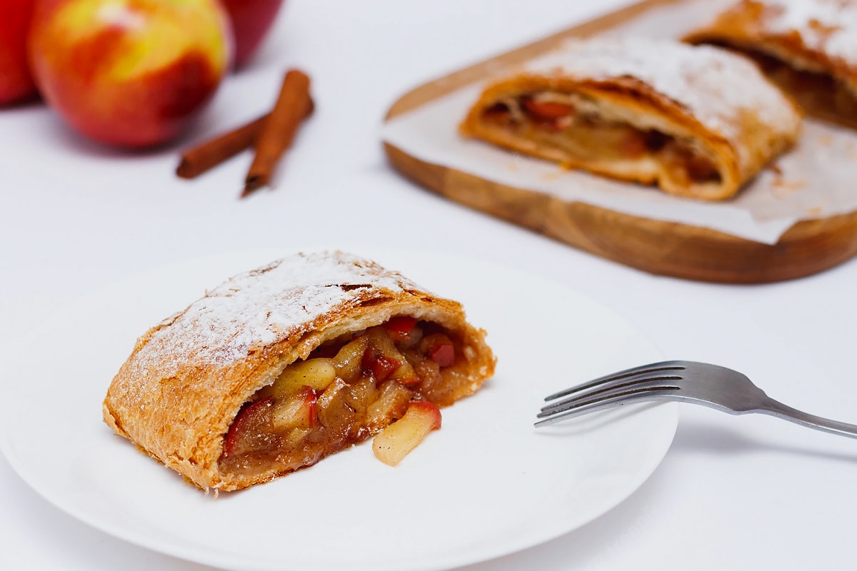 Slice of apple strudel on white plate with fork near.