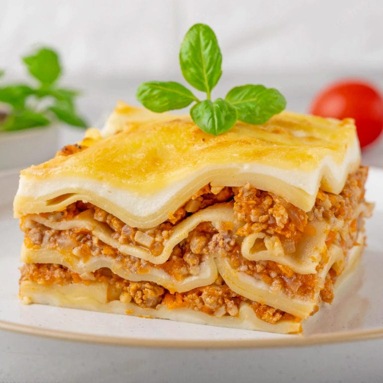 Close look of lasagna slice with basil leaf on a white plate.