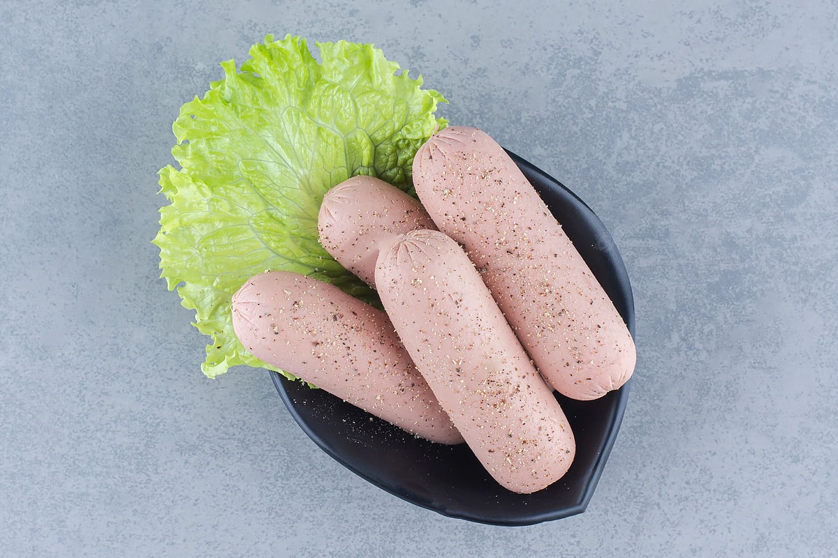 Boiled sausages with salad leaf on a dark plate.