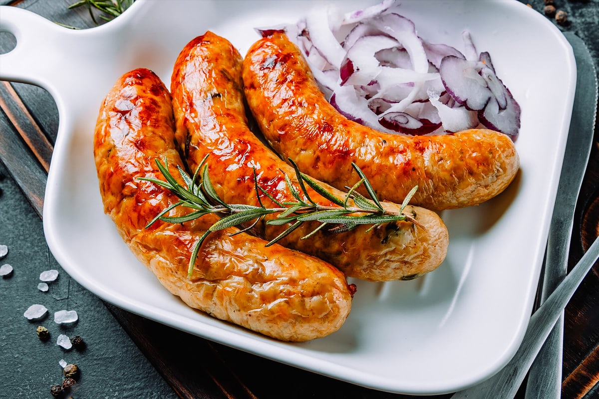 3 Grilled sausages with chopped onions and rosemary brunch on a plate.