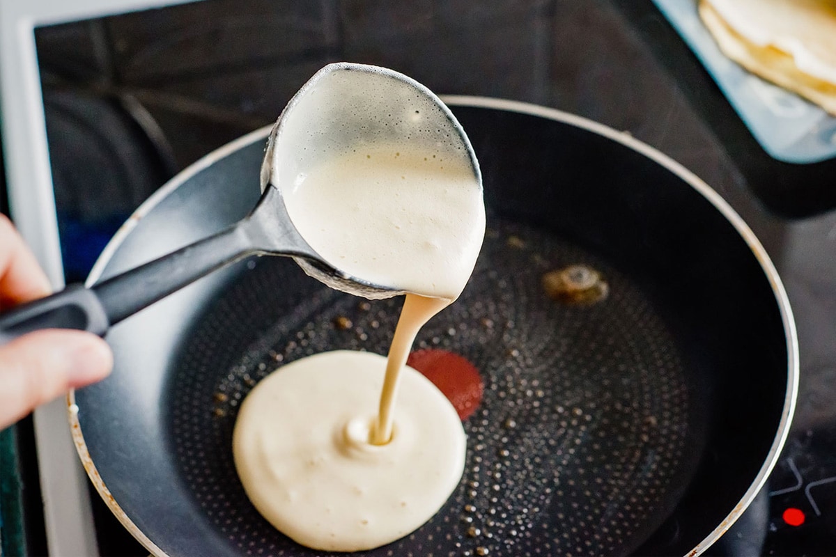 Big spoon pouring pancake mix in a frying pan.