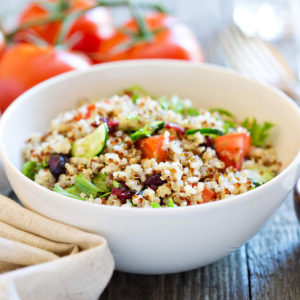 White plate of a quinoa salad with cucumbers, tomatoes and salad.