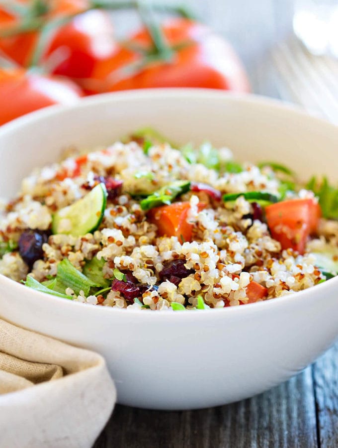 White plate of a quinoa salad with cucumbers, tomatoes and salad.