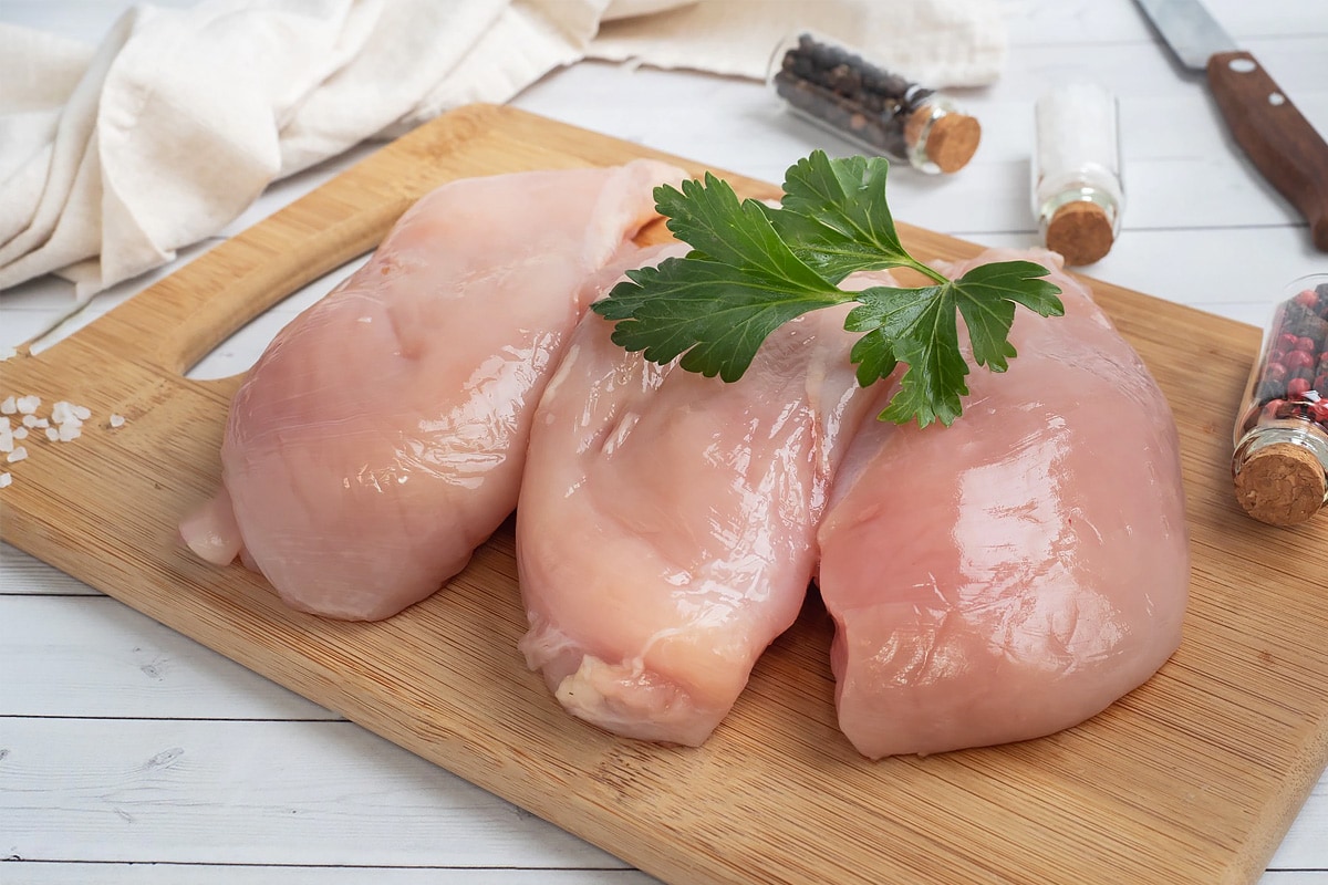 Raw chicken breast sitting on a wooden cutting board with parsley on top.
