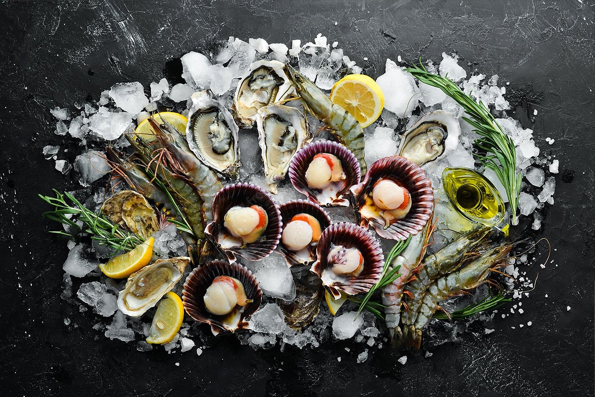 Top view of raw scallops with other seafood on dark background.