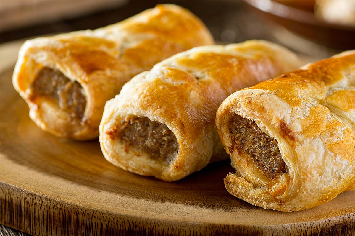 Close look of frozen sausage rolls on a wooden plate.