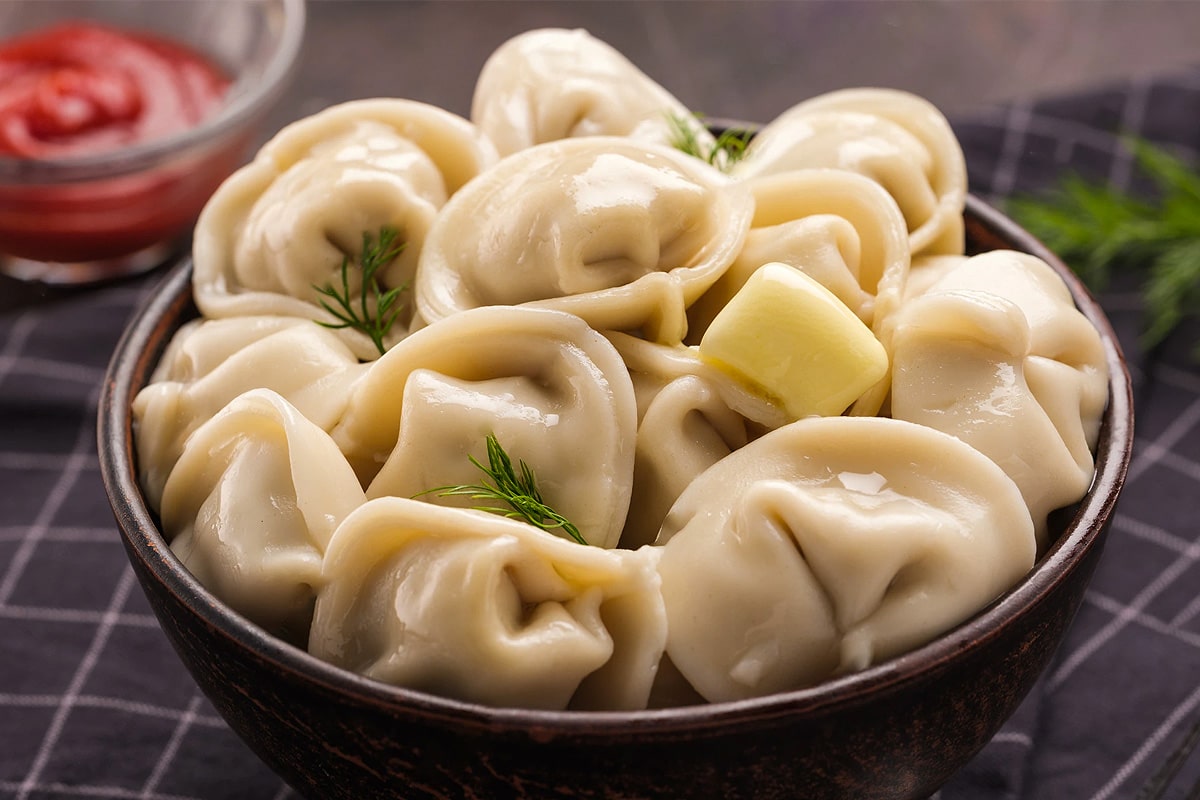 Dark plate with boiled dumplings with a slice of butter and dill leaves.