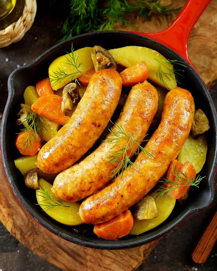 Top view of fried sausages with carrots and potato wedges.