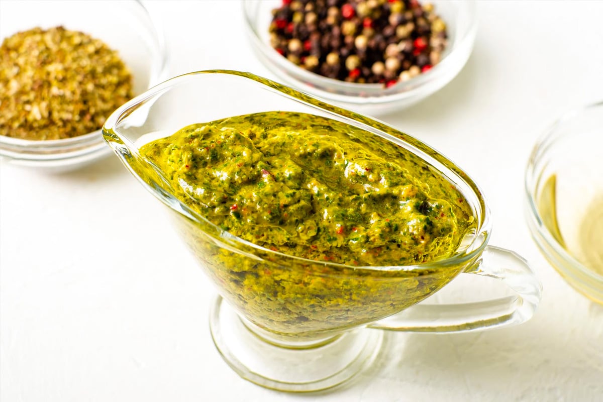 Close look of glass cup full with chimichuri sauce on a white table.