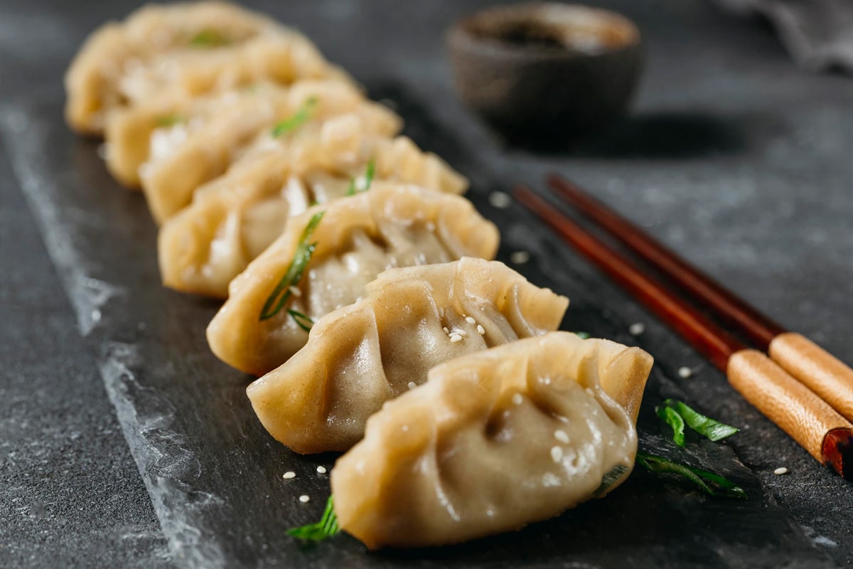 Chinese dumplings on a dark table with chopsticks.