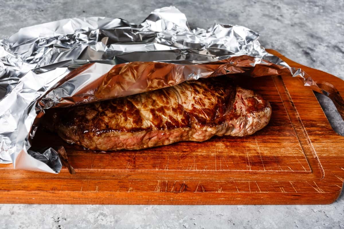 Beef covered with aluminum foil on cutting board.