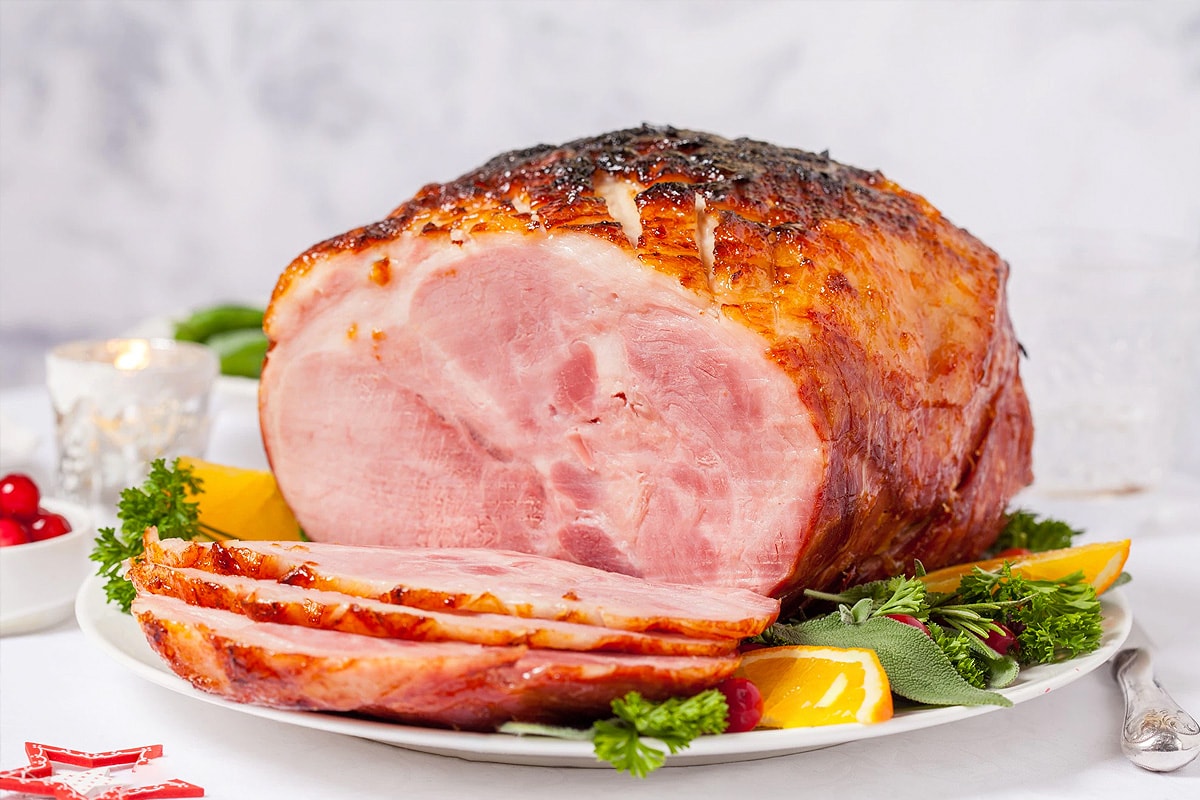 Close look of honey-glazed ham on a white plate with vegetables.