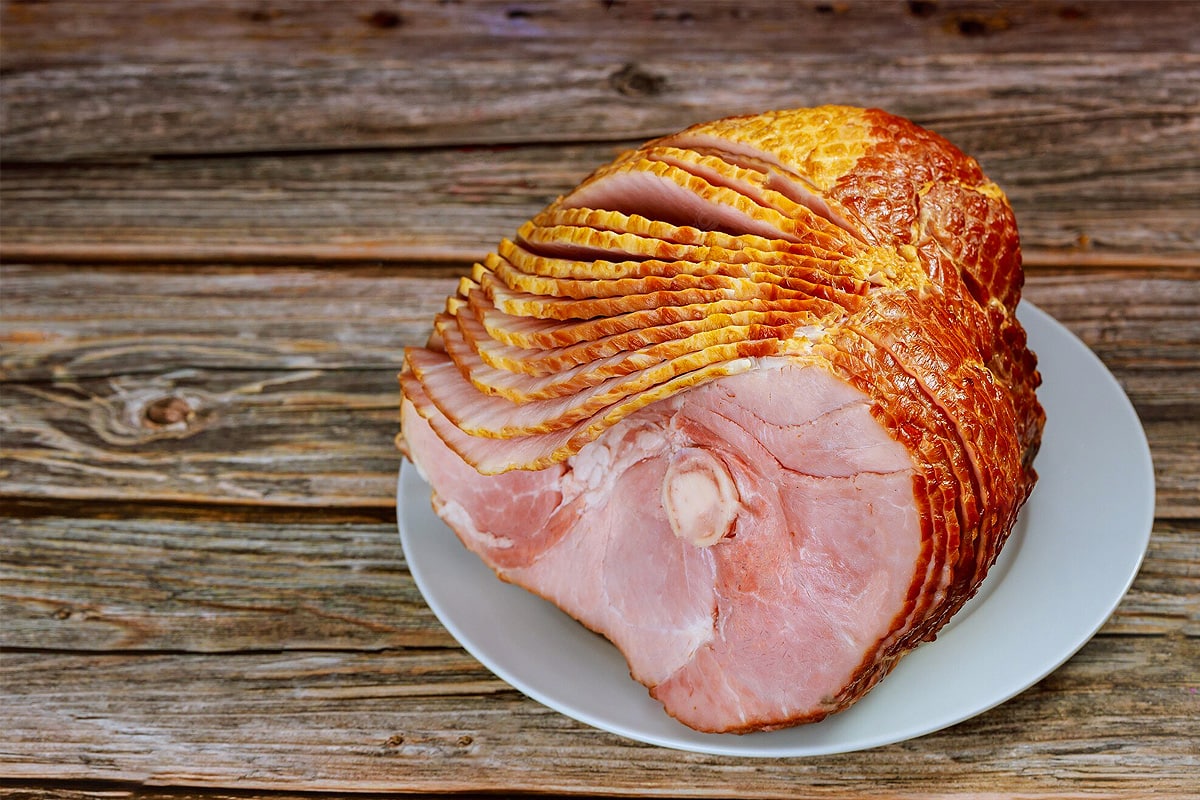 Top view of sliced honey baked ham with bone-in on a wooden table.