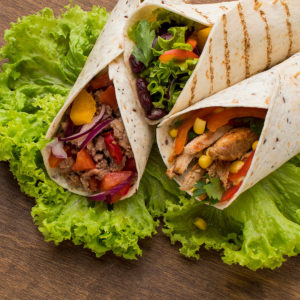 Close look of wraps with corn, tomatoes, onions, chicken and canned beans.
