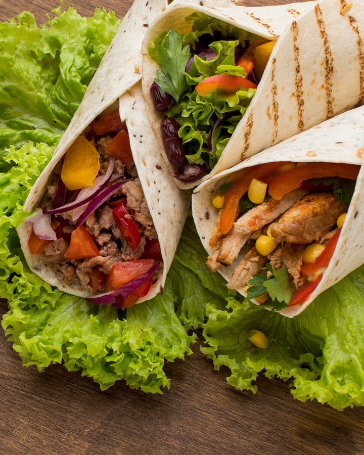 Close look of wraps with corn, tomatoes, onions, chicken and canned beans.