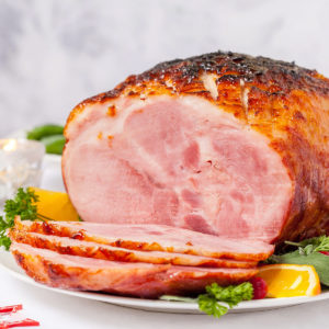 Sliced baked honey-ham on a white plate with orange slices and vegetables.