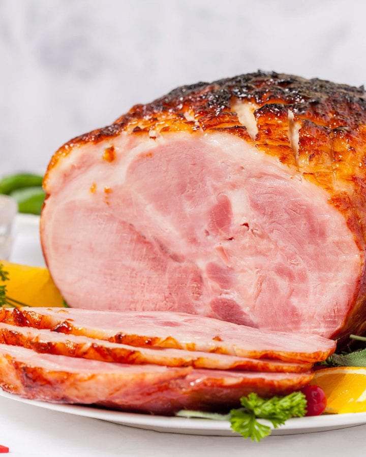 Sliced baked honey-ham on a white plate with orange slices and vegetables.