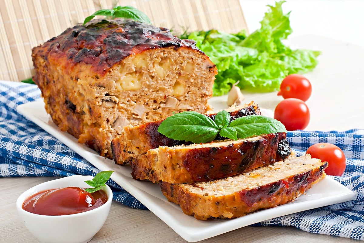 Meatloaf slices on a white table with ketchup and tomatoes.