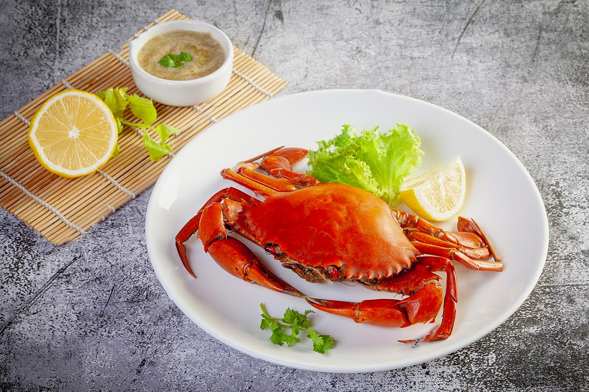 Top view of a big cooked crab in a white plate with lemon and salad leaves.
