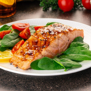 Glazed salmon fillet with sesame seeds on white plate.