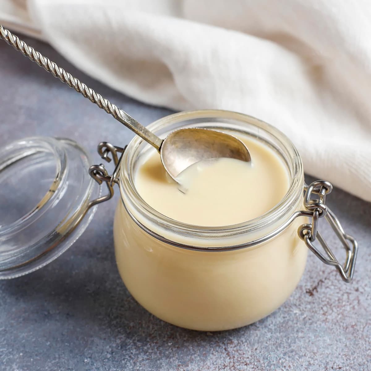 Close look of a glass jar full with condensed milk with a spoon.