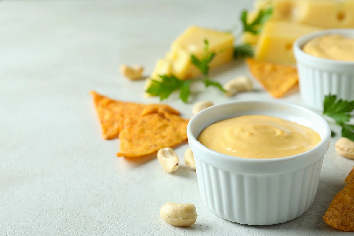 American cheese sauce near some walnuts, nachos and parsley.