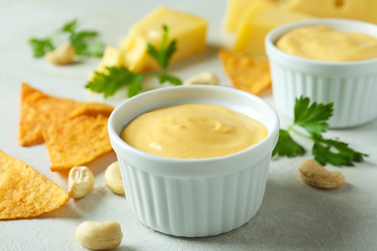 Close look of american cheese sauce near some walnuts, nachos and parsley.