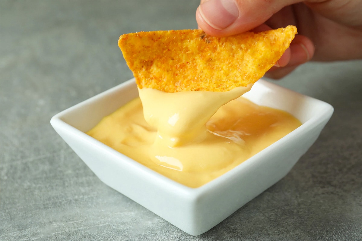 Woman hand dipping a corn nachos in the American cheese sauce.