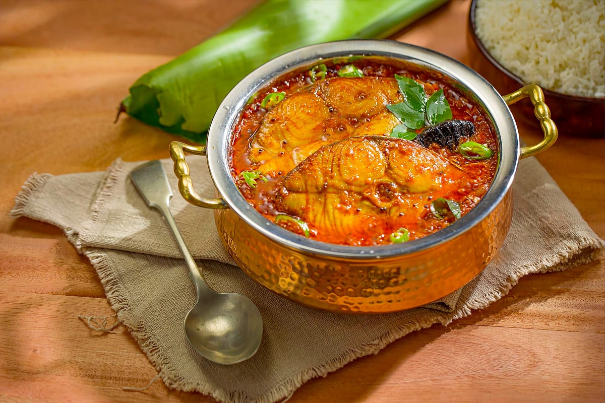 Close view of an Indian bowl with fish curry and spices.