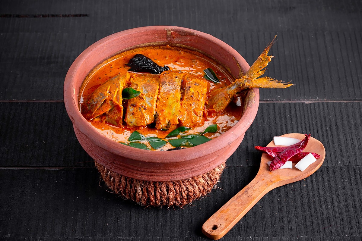 Fish slices in a bowl with fish curry and a wooden spoon.