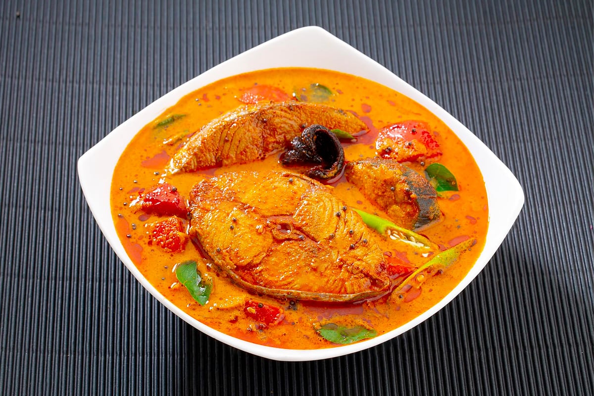 White plate with fish curry on a dark table.
