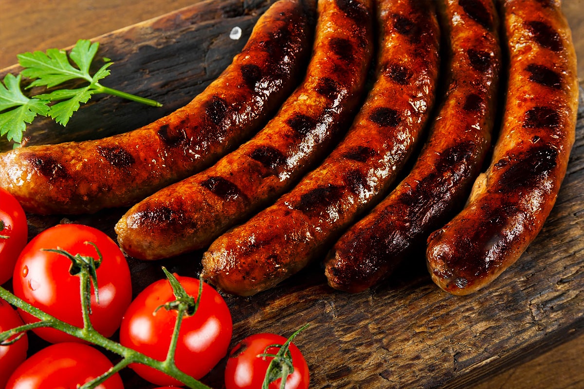 Burnt sausages with fresh tomatoes on a wooden board.