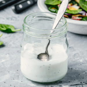 Transparent jar with bleu cheese dressing and a metal spoon.